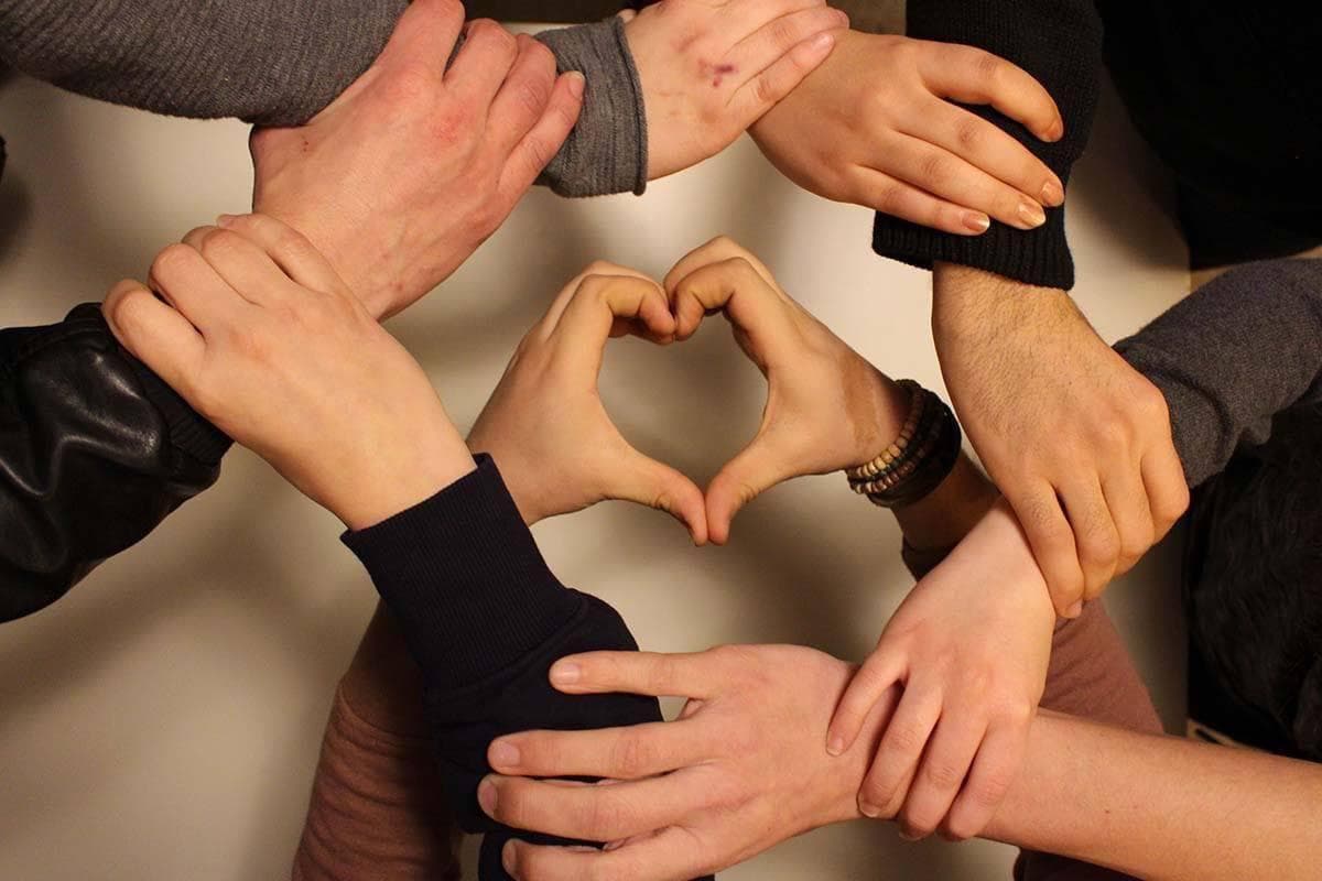 Menschen reichen sich ihre Hände im Kreis und zwei Hände formen in der Mitte des Kreises ein Herz